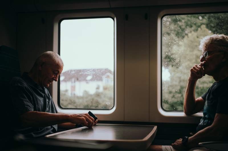 Deux hommes âgés assis côte à côte dans un train regardent par la fenêtre la campagne verdoyante défiler