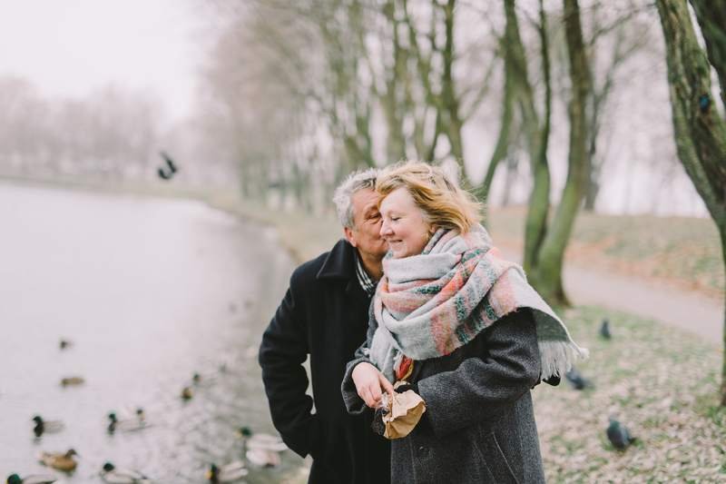 Un couple âgé en manteaux d'hiver s'embrasse tendrement au bord d'un lac, par un jour gris.