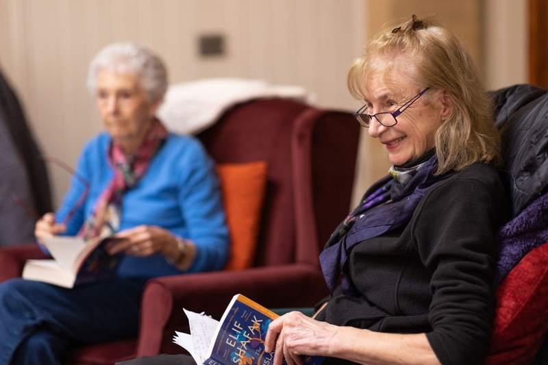 Femmes âgées réunies dans un salon, livres en main, souriantes lors d'une séance de club de lecture