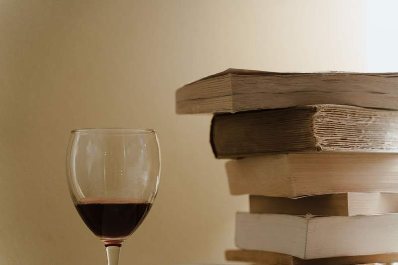 Un verre de vin rouge posé à côté d'une pile de vieux livres, dans une lumière douce et chaude.