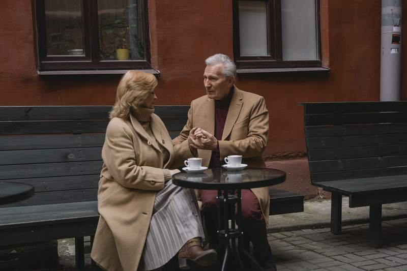 Couple aux cheveux gris attablé à la terrasse d'un café, une tasse à la main, en pleine conversation détendue