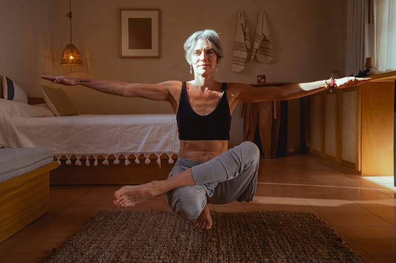 Femme âgée tenant une posture d'équilibre de yoga dans sa chambre, exercice doux pratiqué à la maison