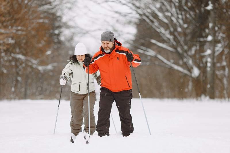 Un couple pratique le ski de fond côte à côte sur une piste enneigée bordée d'arbres.