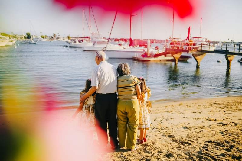 Des grands-parents et leurs petites-filles debout au bord de la mer par une journée ensoleillée, des bateaux au loin