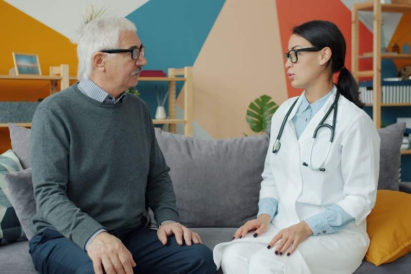 Un homme âgé écoute une médecin lors d'une consultation dans un cabinet coloré.